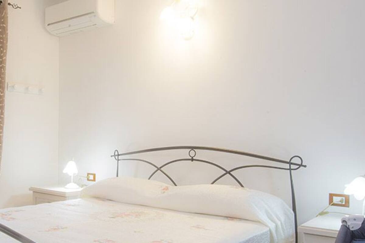A bedroom with a bed, curtains, bedside lamps, and a wall-mounted air conditioner.