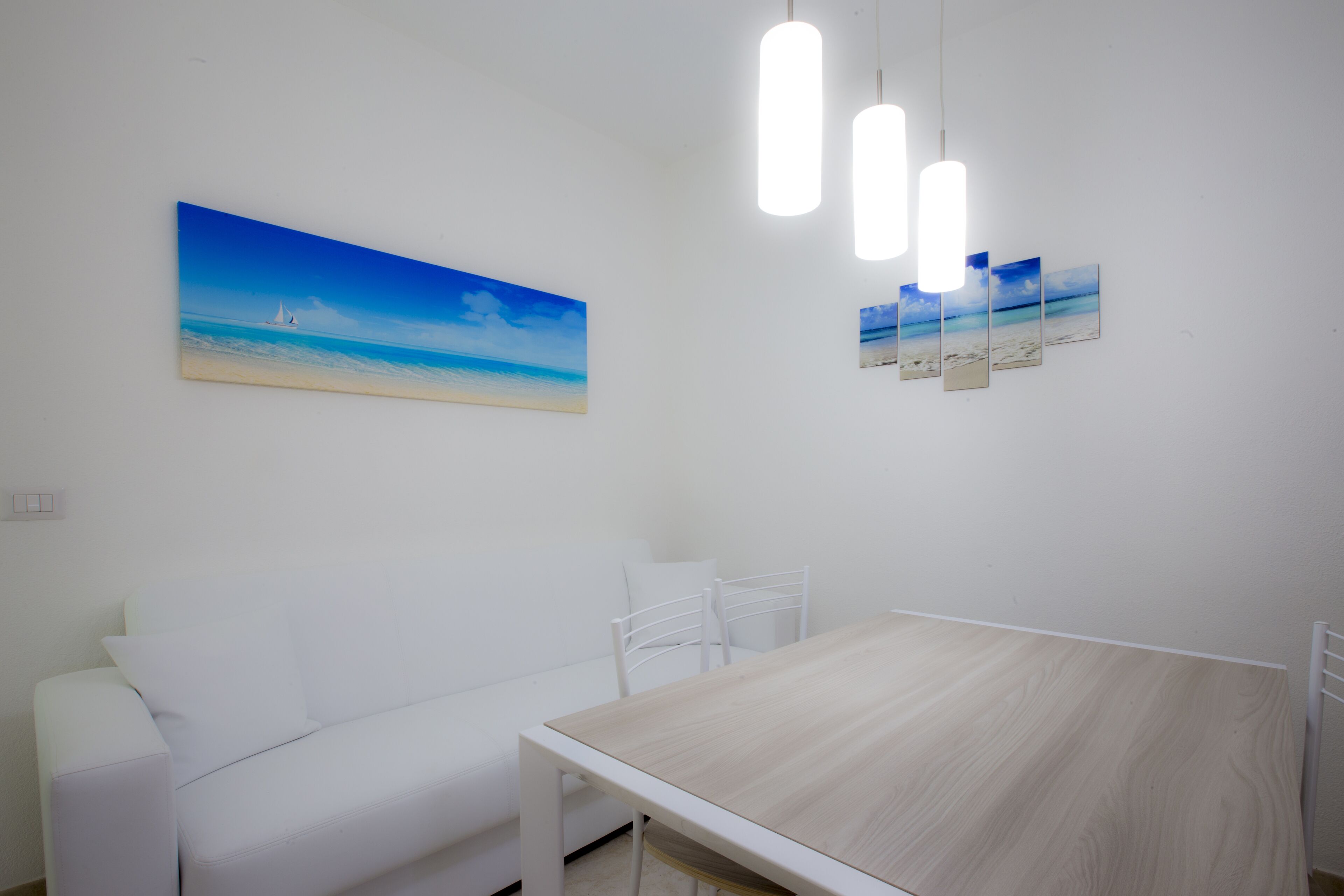 A minimalist room with a wooden table, white chairs, a white sofa, and a wall-mounted painting of a beach scene.