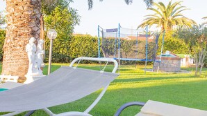 Uma área de piscina com espreguiçadeira, palmeiras e um espaço de recreação cercado.