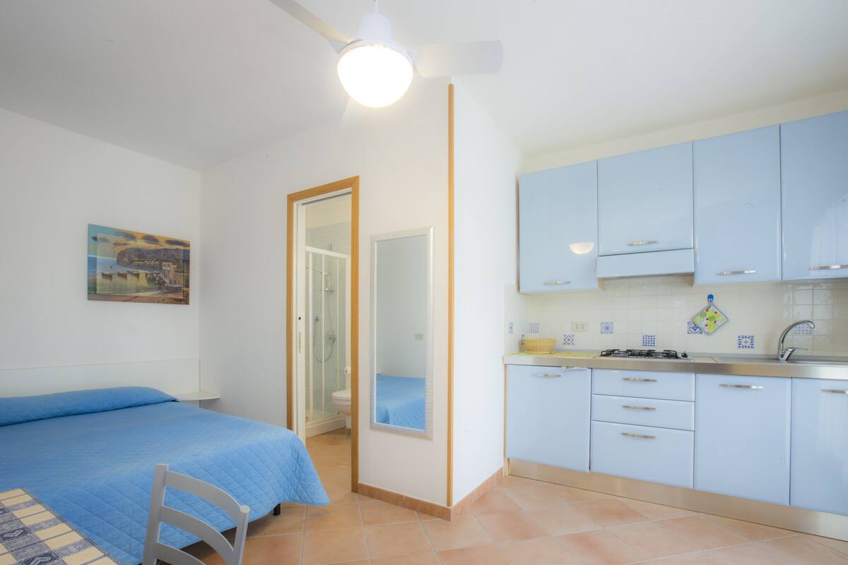 A bedroom with a bed, a chair, and a bathroom with a shower.