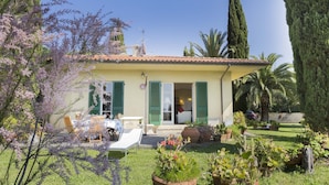 A house with a garden, a patio with chairs and a table, and a car parked nearby. - Villa Lilla (Portoferraio)