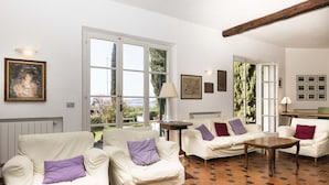 A spacious living room with two white sofas, a wooden coffee table, and a large window providing a view of greenery. - Villa Lilla (Portoferraio)