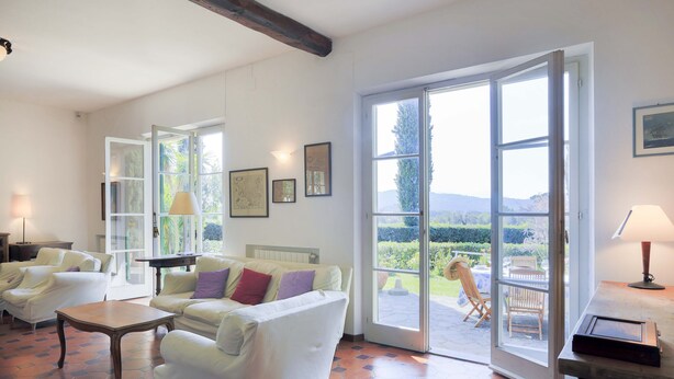 A spacious living room with a large sliding glass door leading to an outdoor area, white furniture, and a tiled floor. - Villa Lilla (Portoferraio)