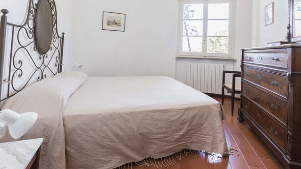Une chambre à coucher avec un lit, une commode, une fenêtre, un radiateur et un tableau accroché au mur.