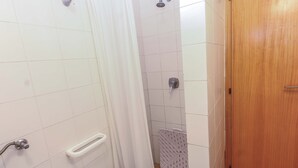 Un baño con paredes de azulejos blancos, ducha, inodoro y puerta de madera.