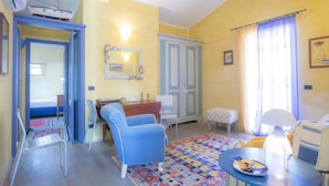 A room with a bed, a desk, a chair, a small table with a lamp, and a colorful rug. - Terrazza Ferdinando (Porto Azzurro)