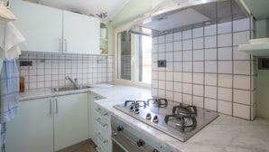 A kitchen with white cabinets, a gas stove, and a window. - Terrazza Ferdinando (Porto Azzurro)