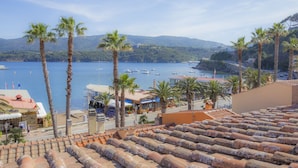 A coastal view with a terracotta-tiled roof, palm trees, and boats on the water. - Terrazza Ferdinando (Porto Azzurro)