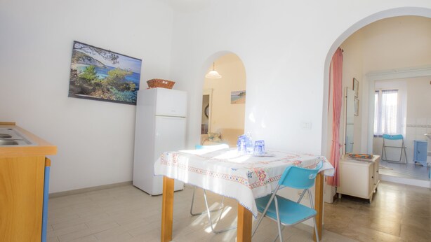 Un comedor con una mesa lista para dos personas, un refrigerador y una cocina visible a través de un arco.