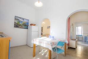 Un comedor con una mesa lista para dos personas, un refrigerador y una cocina visible a través de un arco.