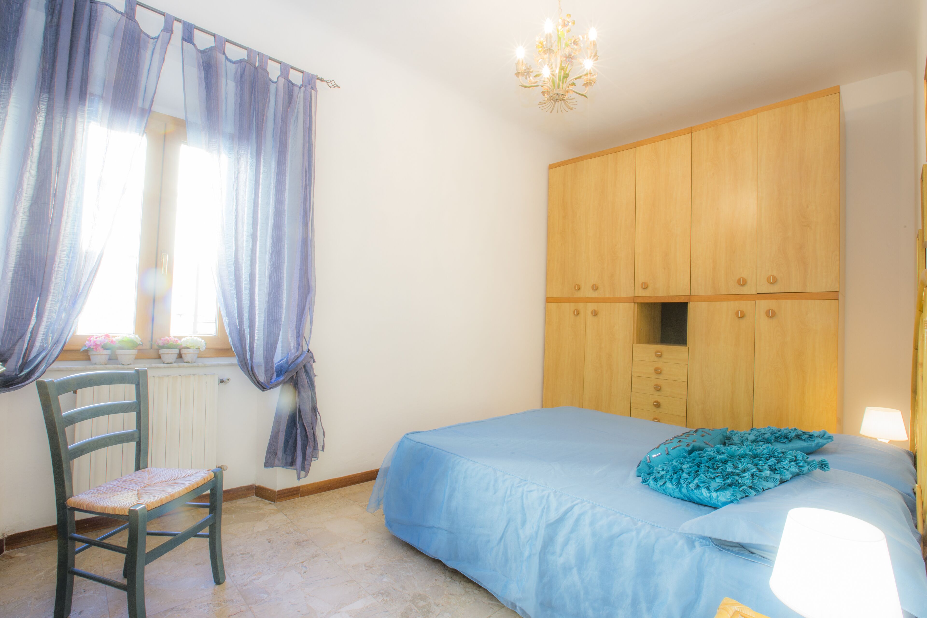 A bedroom with a bed, a chair, a wardrobe, a radiator, and a window with curtains.