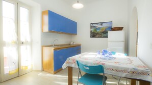Cocina compacta con armarios azules, un refrigerador blanco y una mesa de comedor con mantel estampado.