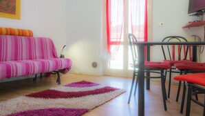 Uma sala de estar com um sofá listrado, uma mesa de jantar com cadeiras vermelhas e uma janela grande com cortinas vermelhas.