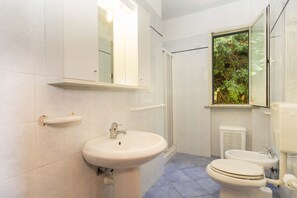 Casa de banho com lavatório, sanita e janela com vista para vegetação.