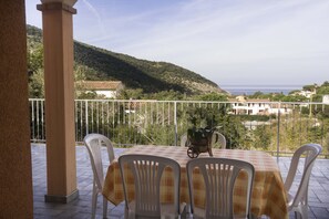 Terraço com mesa e cadeiras, com vista para uma paisagem montanhosa e o litoral.