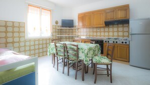 A compact kitchen with wooden cabinets, a dining table with chairs, a television, and a refrigerator. - Appartameno Mediterraneo (Campo nell'Elba)