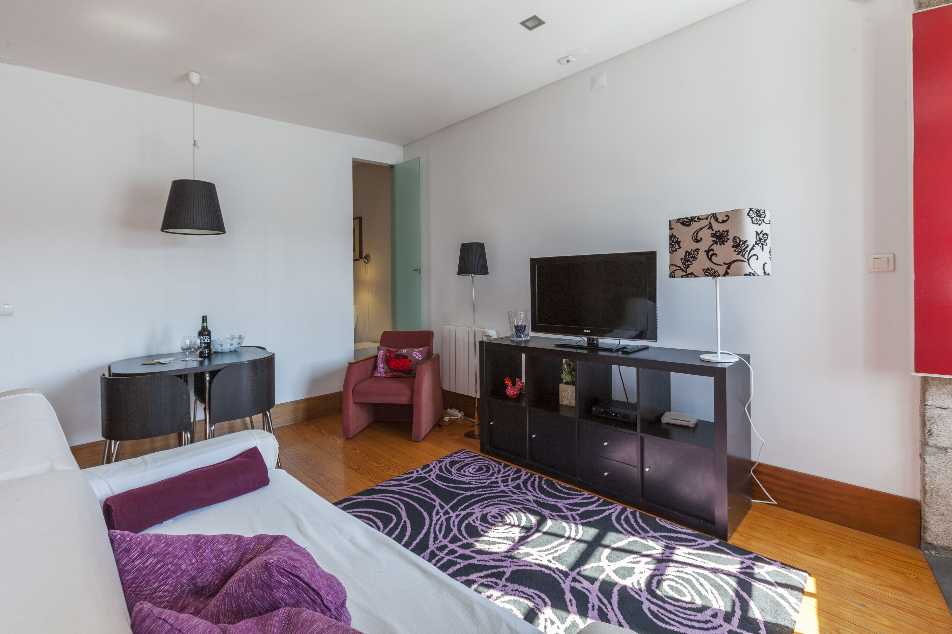 A modern hotel room with a bed, a desk, a chair, a TV, and a lamp.