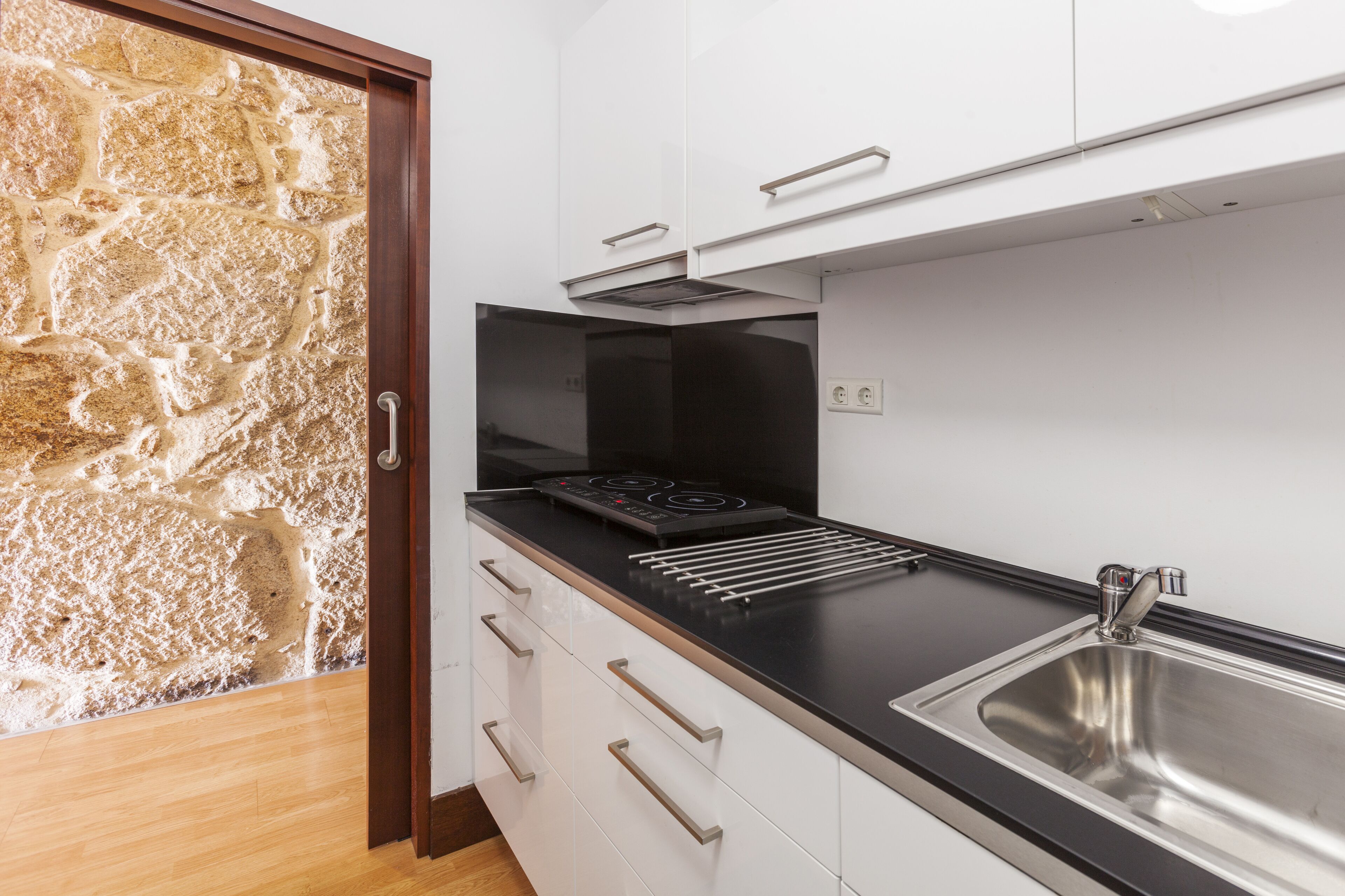 A modern kitchen with white cabinets, a black countertop, and a stainless steel sink.