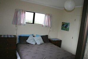A bedroom with a bed, two nightstands, a dresser, a window with curtains, and a wall-mounted painting.
