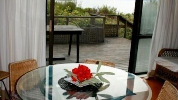 A round glass table with a floral centerpiece, surrounded by wicker chairs. - Nestled Atop the Lane - Pukawa Bay Holiday Home (Pukawa Bay)