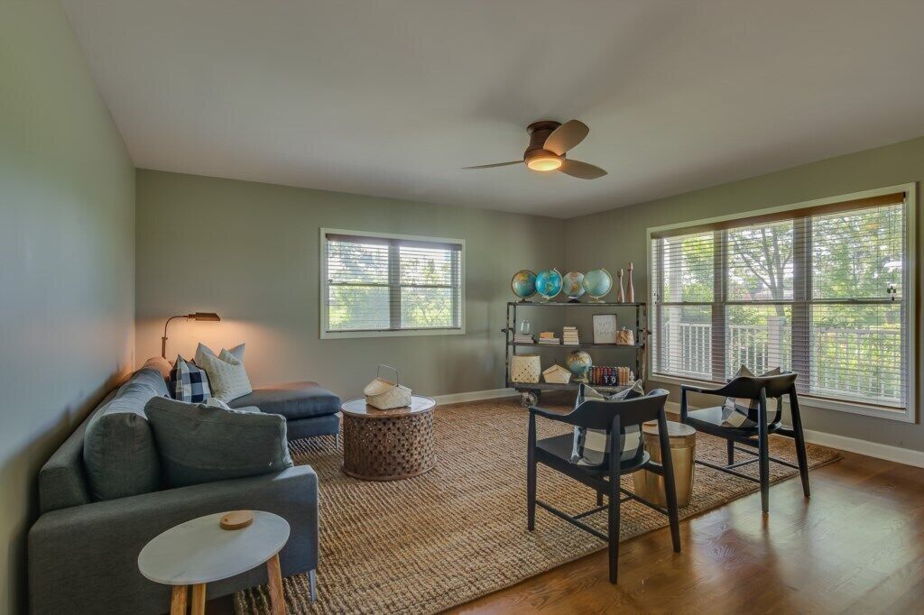 A living room with a sofa, chairs, a coffee table, a bookshelf, and a ceiling fan.