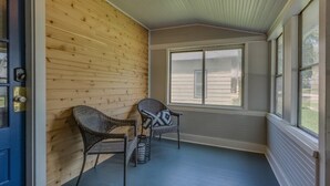 Eine überdachte Veranda mit zwei Korbstühlen und einem kleinen Tisch, Holzwänden und großen Fenstern.