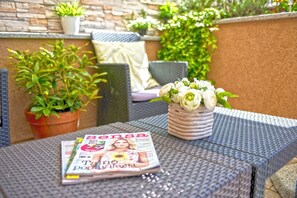Un magazine sur une table, une plante en pot et un coussin, le tout dans un décor extérieur.