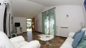 A spacious living area with a white sofa, a small round table, and a television on a cabinet. - Villa Raffaella (Massa Lubrense)