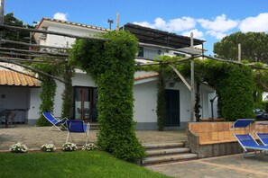 A building with a tiled roof, a staircase leading to a door, and two blue lounge chairs in the foreground. - Villa Raffaella (Massa Lubrense)