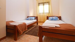 A small, clean room with two single beds, a window with yellow curtains, and a brown rug on the floor.
