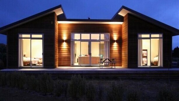 A modern two-story house with large sliding glass doors on the ground floor, a patio area, and a visible bedroom with a bed and nightstand. - Carrot Cake Chalet - Ohakune (Ohakune)