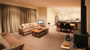 A living room with a sofa, coffee table, and TV. There is a kitchen area with a stove and dining table. - Carrot Cake Chalet - Ohakune (Ohakune)
