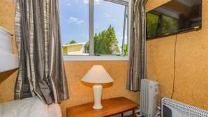 Une chambre d’hôtel avec un lit, une table avec une lampe, un téléviseur fixé au mur et une fenêtre avec des rideaux.