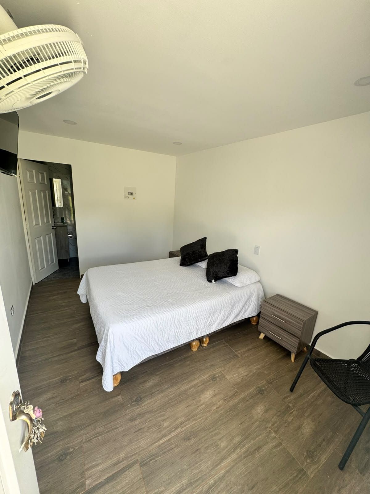 A bedroom with a bed, a nightstand, a chair, and a door leading to a bathroom.