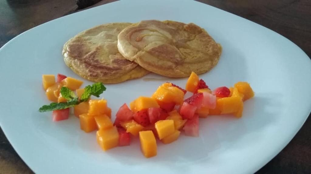 A plate with two pancakes and a fruit salad.