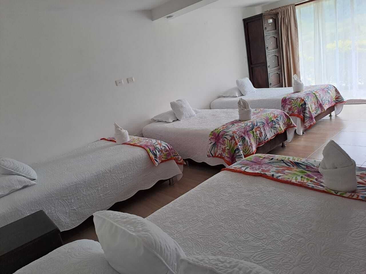 A hotel room with three single beds, each with a white bedspread and a colorful floral blanket.
