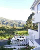 A modern building with a white exterior, a balcony, and a view of a green valley with mountains in the background.