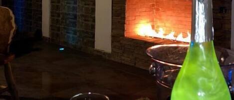 Una habitación con chimenea de ladrillo, una mesa con dos vasos y una botella, y una silla.