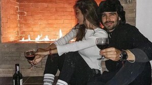 Deux personnes sont assises sur le sol, tenant des verres à vin, avec une cheminée en arrière-plan.