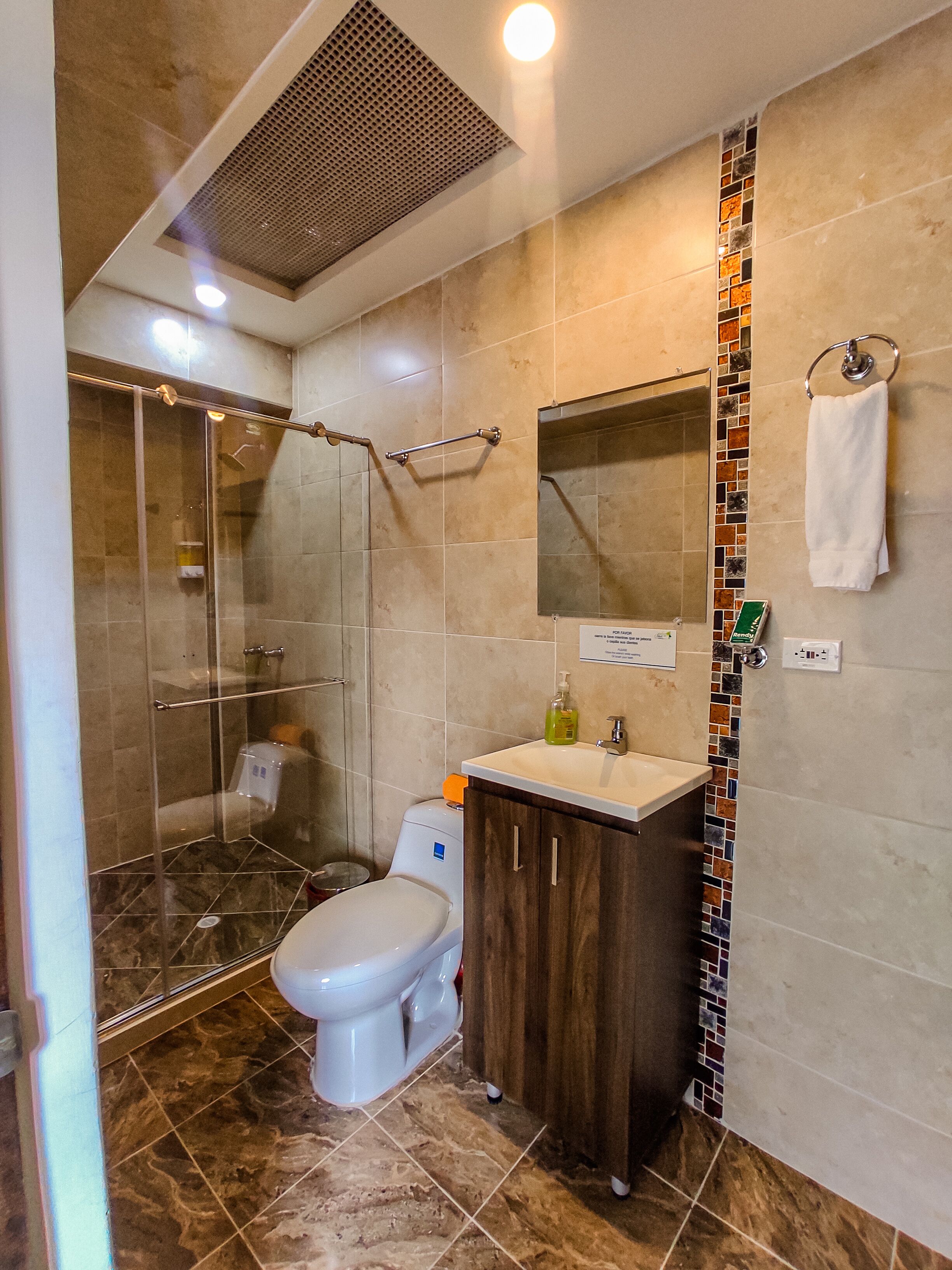 Un baño moderno con ducha envuelta en vidrio, inodoro blanco, tocador de madera y salpicadero de azulejos.