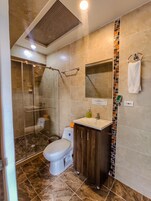 Un baño moderno con ducha envuelta en vidrio, inodoro blanco, tocador de madera y salpicadero de azulejos.