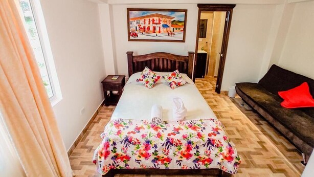 Une chambre à coucher bien rangée, avec un lit, un canapé, un tableau au mur et une fenêtre avec des rideaux.