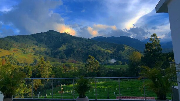 Un balcon offrant une vue sur des collines verdoyantes et une chaîne de montagnes sous un ciel partiellement nuageux.