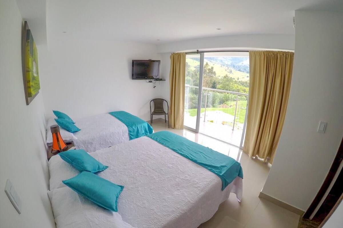 Habitación de hotel con dos camas, televisión y balcón con cortinas.
