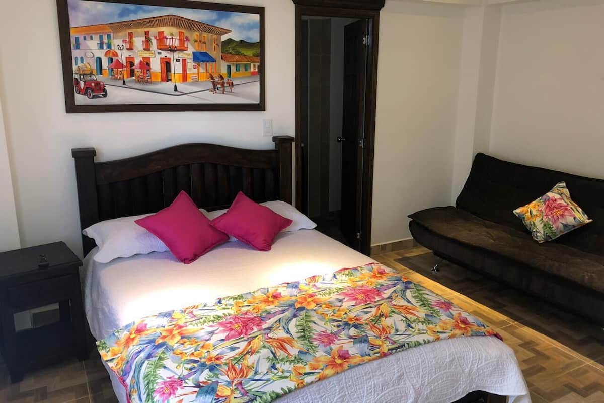 Un dormitorio con cama, mesita de noche, sofá y un cuadro en la pared.