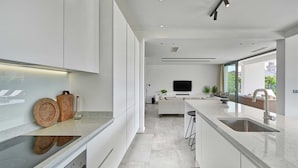 A modern kitchen with white cabinetry, a large island with a sink, and a dining area with a TV.