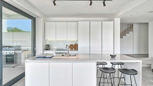 A modern kitchen with a central island, bar stools, and a view of the outdoors.