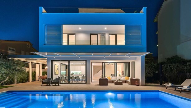 A modern two-story house with a swimming pool in the foreground.