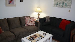 A living room with two sofas, a coffee table, a lamp, and wall decorations. - Cozy Efficiency near University and town (BROWNWOOD)