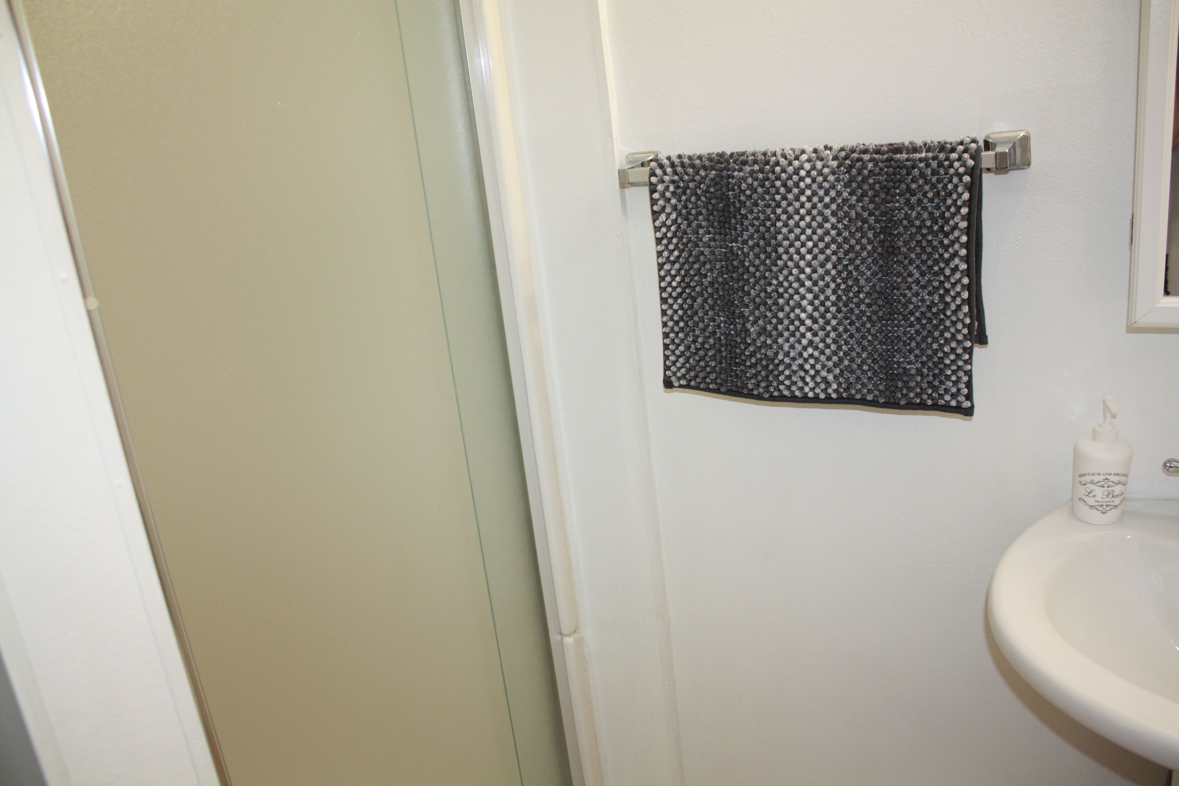 Une salle de bain avec un lavabo blanc, une serviette suspendue à un porte-serviettes et un flacon de savon liquide.